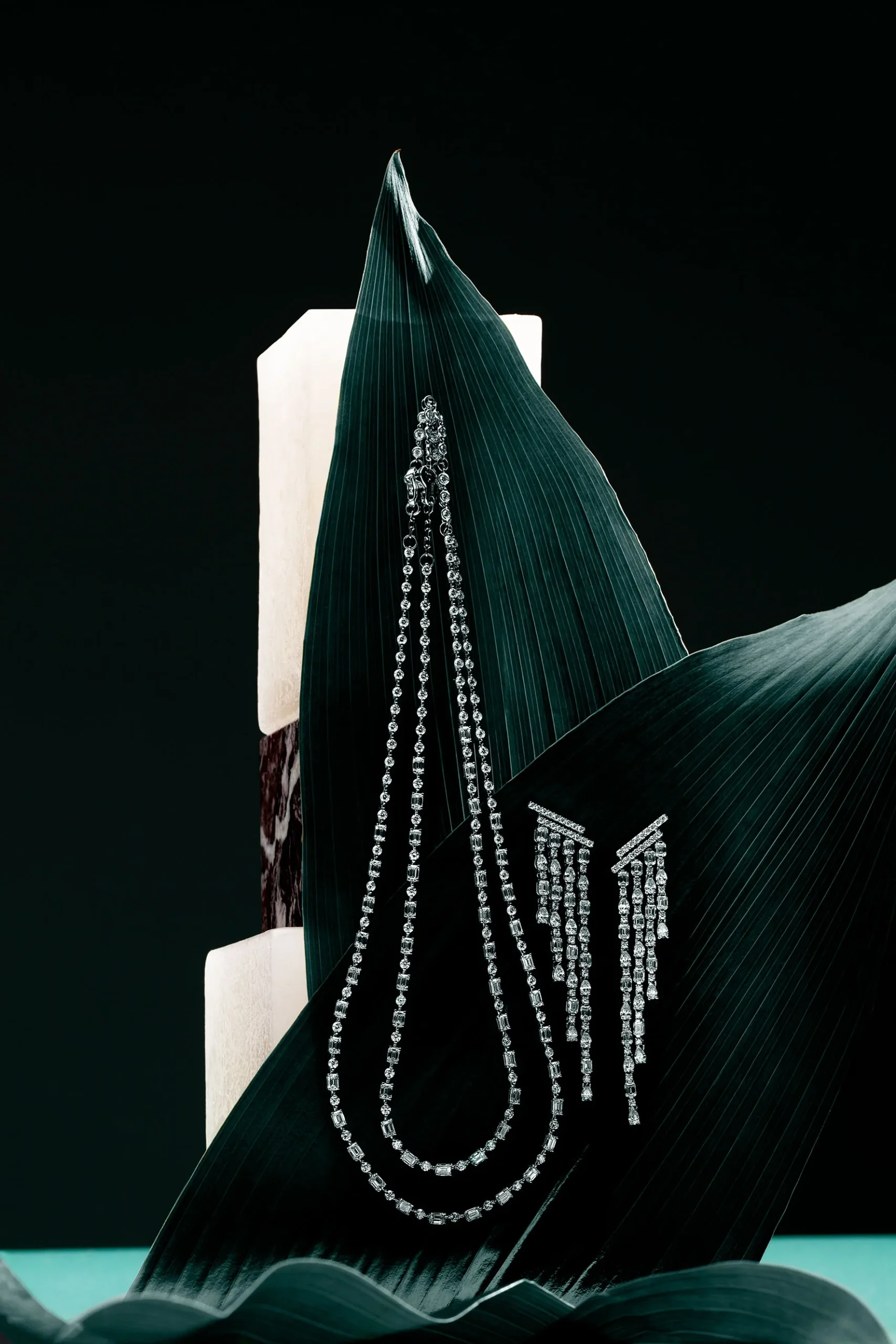 Long diamond necklaces and earrings on a dark green leaf